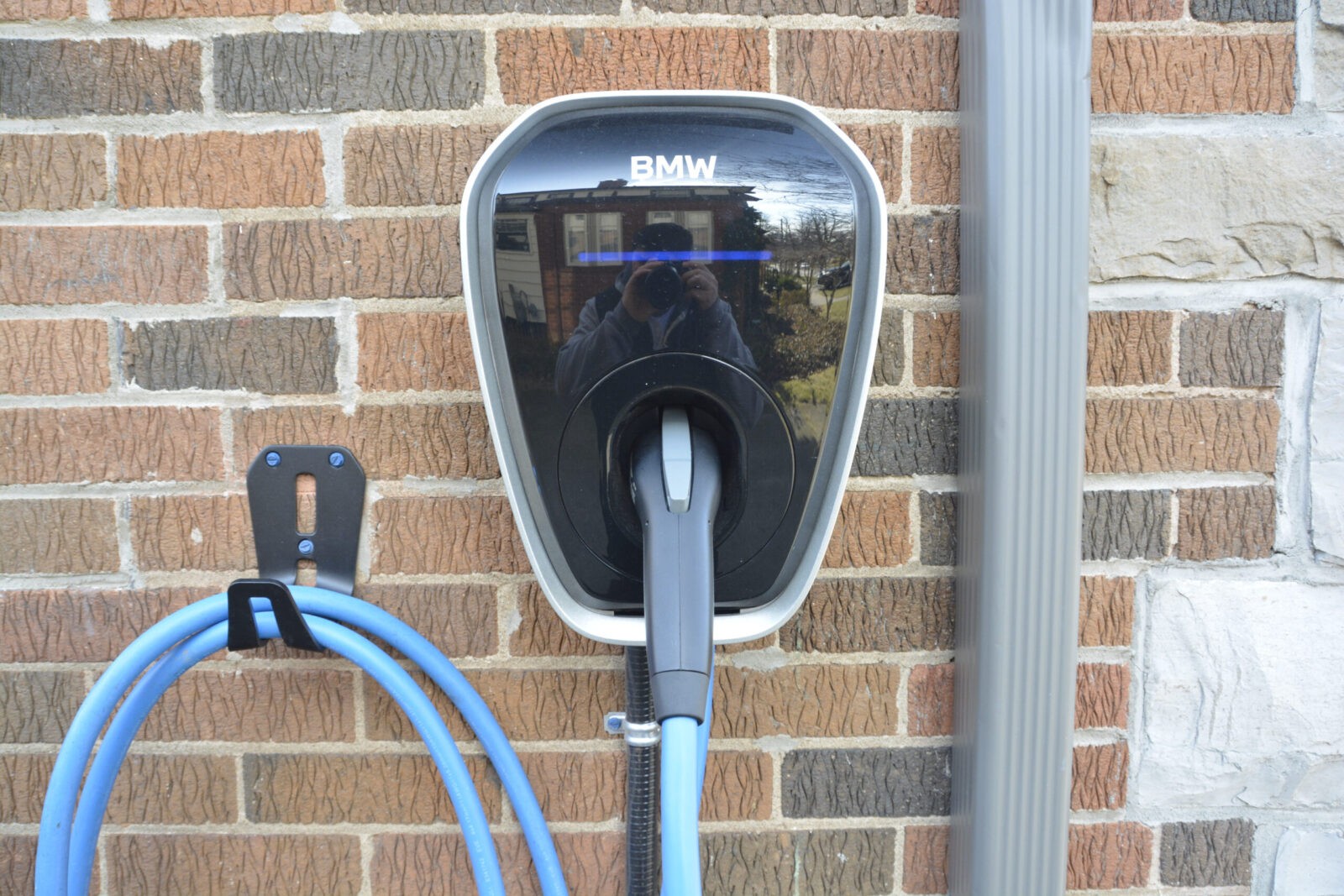 _DSC0040 A black electrical vehicle charging unit with a blue power cord against a brick wall.
