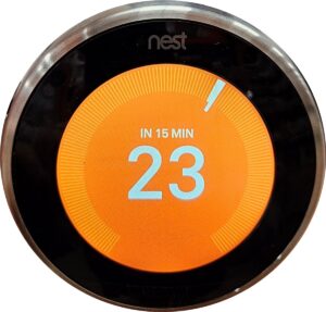 A thermostat showing 23 degrees Celsius. The screen is orange indicating that there is heat being produced.